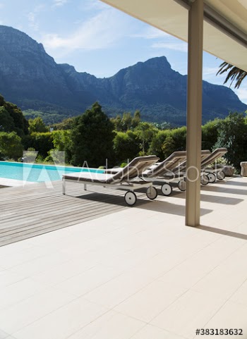 Lounge chairs lined up at sunny resort swimming pool below mountains