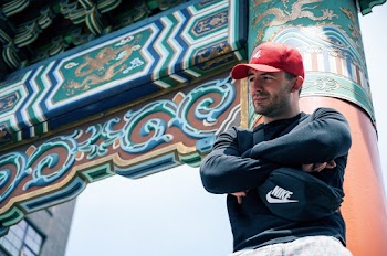 Low Angle Photo of Man Leaning on Red Chinese Pillar Posing With His Arms Crossed Looking Away