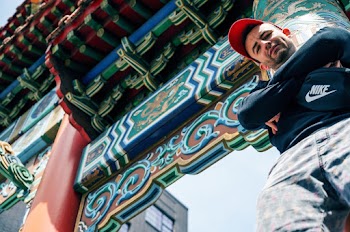 Low Angle Photo of Man Leaning on Red Chinese Pillar Posing With His Arms Crossed Looking Down