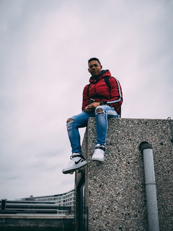 Low Angle Photo of Man Sitting at the Edge of a Stone Wall of a Building