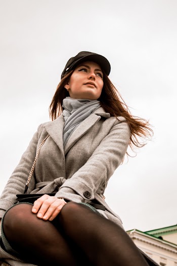 Low Angle Photo of Sitting Woman in Gray Coat and Black Hat Posing While Looking Away