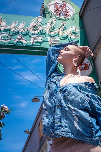 Low Angle Photo of Woman in Blue Denim Jacket Posing Under Cafe Signage