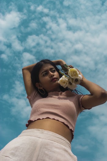 Low Angle Photo of Woman in Peach Short-sleeved Crop Top Holding White Roses Posing Under Blue Sky