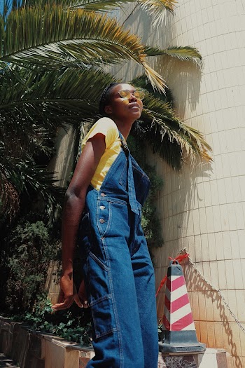 Low Angle Photo of Woman In Yellow T-shirt, Sunglasses and Blue Dungarees Posing While Looking Down