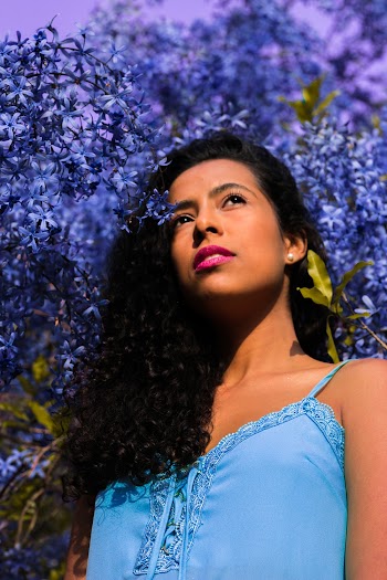 Low Angle Photo of Woman Standing Near Blue-Petaled Flowers