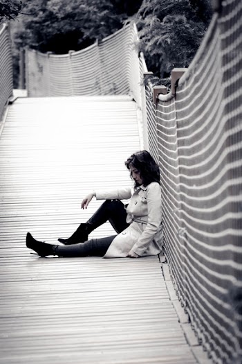 Low Light Photo of Woman Wearing Trench Coat Sitting Against Wall