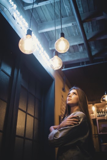 Low Light Photography of Woman Standing Under Chandelier