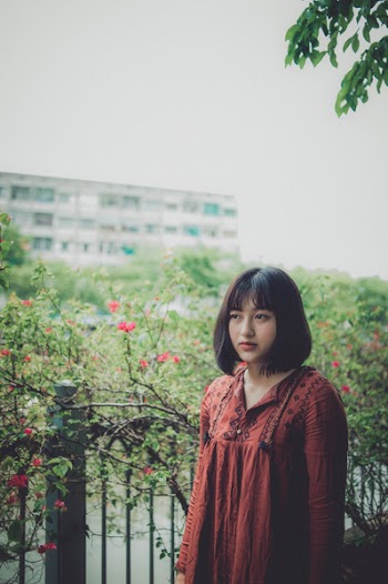 Lowlight Photography of Woman in Red Shirt Standing Beside Plant