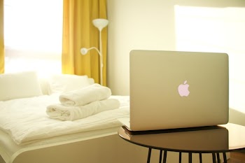 Macbook Air on Top of Wooden Table Facing White Bed