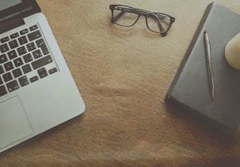 Macbook Pro Beside Black Framed Eyeglasses on Brown Wooden Surface
