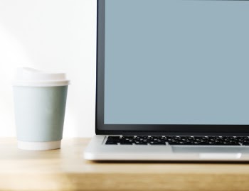 Macbook Pro Beside Gray Disposable Cup on Brown Wooden Surface