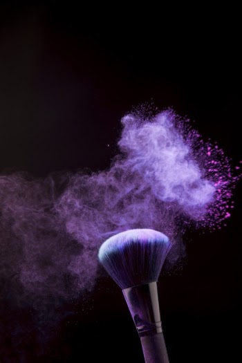 Makeup brush in mist of powder on dark background Free Photo