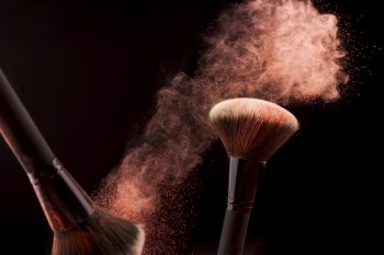 Makeup brushes in dust of red powder on dark background Free Photo
