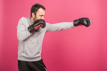 Male boxer training in box gloves, isolated on pink