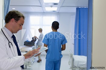 Male doctor using digital tablet making rounds in hospital