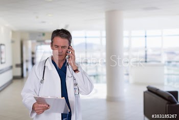 Male doctor with clipboard talking on smart phone in hospital lobby