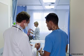 Male doctors discussing medical chart in hospital room doorway