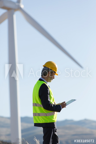 Male engineer examining wind turbine on sunny wind farm