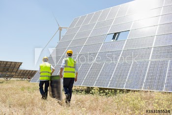 Male engineers fixing solar panel in sunny field with wind turbine