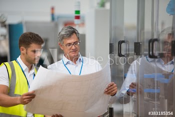 Male engineers looking at blueprints in factory