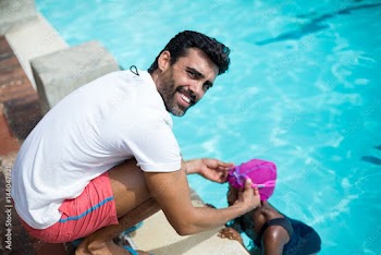 Male instructor assisting girl at poolside