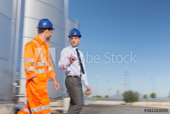 Male manager and worker talking below storage tank