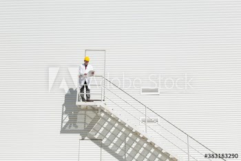 Male manager in lab coat standing outside sunny dairy farm building