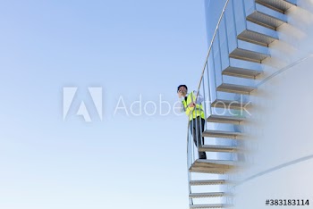 Male manager using walkie talkie on storage tank stairs