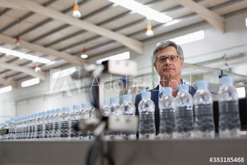 Male manager watching water bottles on factory production line