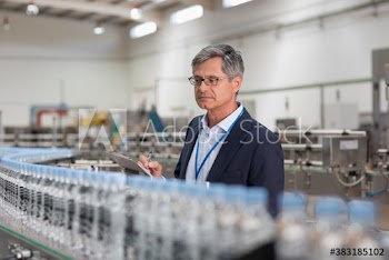 Male manager with clipboard supervising water bottle production line