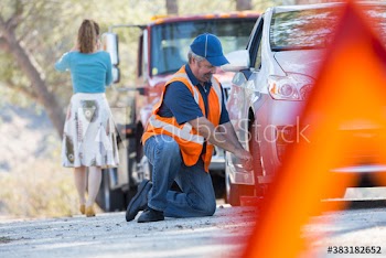 Male roadside assistance mechanic changing tire for woman at roadside