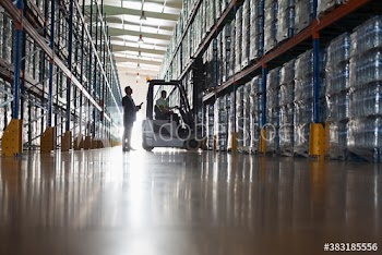 Male supervisor and worker operating forklift in distribution warehouse