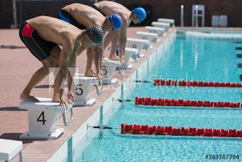Male swimmers poised on starting blocks above sunny swimming pool