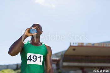 Male track and field athlete drinking sports drink on sunny field