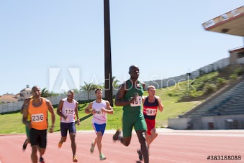 Male track and field athlete racing on sunny running track