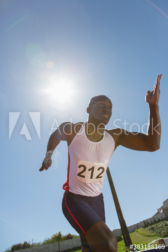 Male track and field athlete sprinting on sunny running track