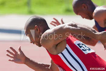 Male track and field athlete sprinting on sunny running track