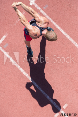 Male track and field athlete stretching arms on sunny running track