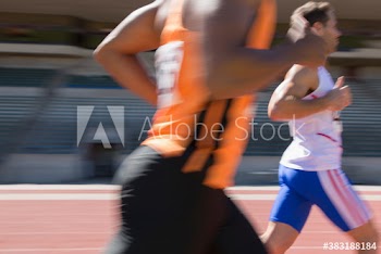 Male track and field athletes racing on sunny running track