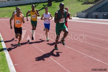 Male track and field athletes racing on sunny running track