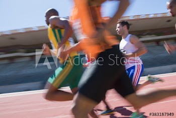 Male track and field athletes racing on sunny sports track