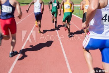 Male track and field athletes running on sunny running track
