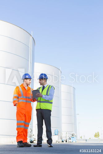 Male worker and manager talking below storage tanks on dairy farm