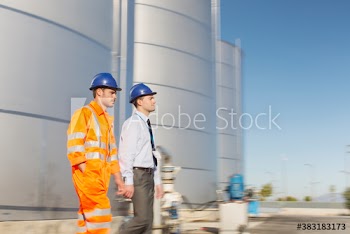 Male worker and manager walking below storage tanks