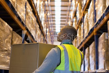 Male worker carrying box in aisle of distribution warehouse
