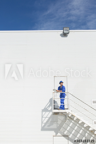 Male worker in coveralls on staircase outside sunny building
