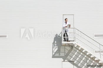 Male worker in lab coat on staircase outside sunny dairy farm building