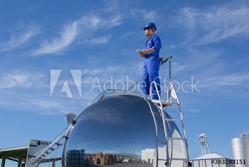 Male worker standing on top of milk tanker on sunny dairy farm