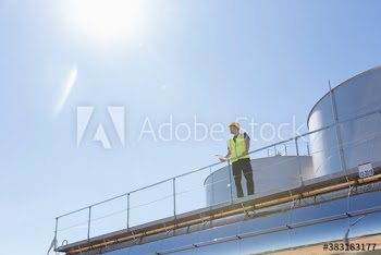 Male worker standing on top of milk tanker on sunny dairy farm