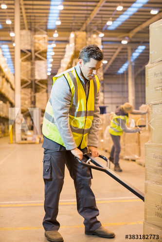 Male worker using pallet jack in distribution warehouse